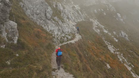 vista trasera de dos excursionistas caminando por el camino de la montaña resegone en el norte de italia con niebla en el fondo en un día de niebla