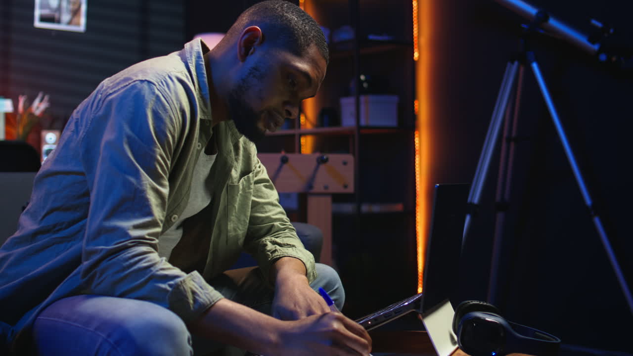 Vertical Video Black freelancer taking notes on his textbook in order to solve his tasks
