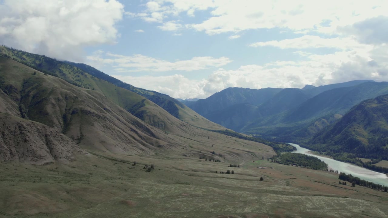 Riprese con drone di aspre creste montuose e paesaggio di valle verde sotto nuvole drammatiche nella Valle di Ak-Kem, Repubblica dell'Altai, Russia, scenario di natura selvaggia remota.