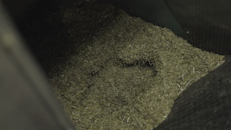 close-up of processed yerba mate (ilex paraguariensis) leaves and stems inside an industrial grinder during the final grinding phase for infusion preparation, showing powder texture, slow motion.