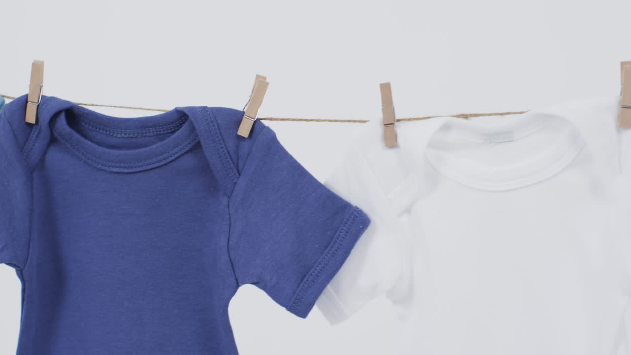 Video of multi coloured baby grows hanging on pegs from line with copy space on white background