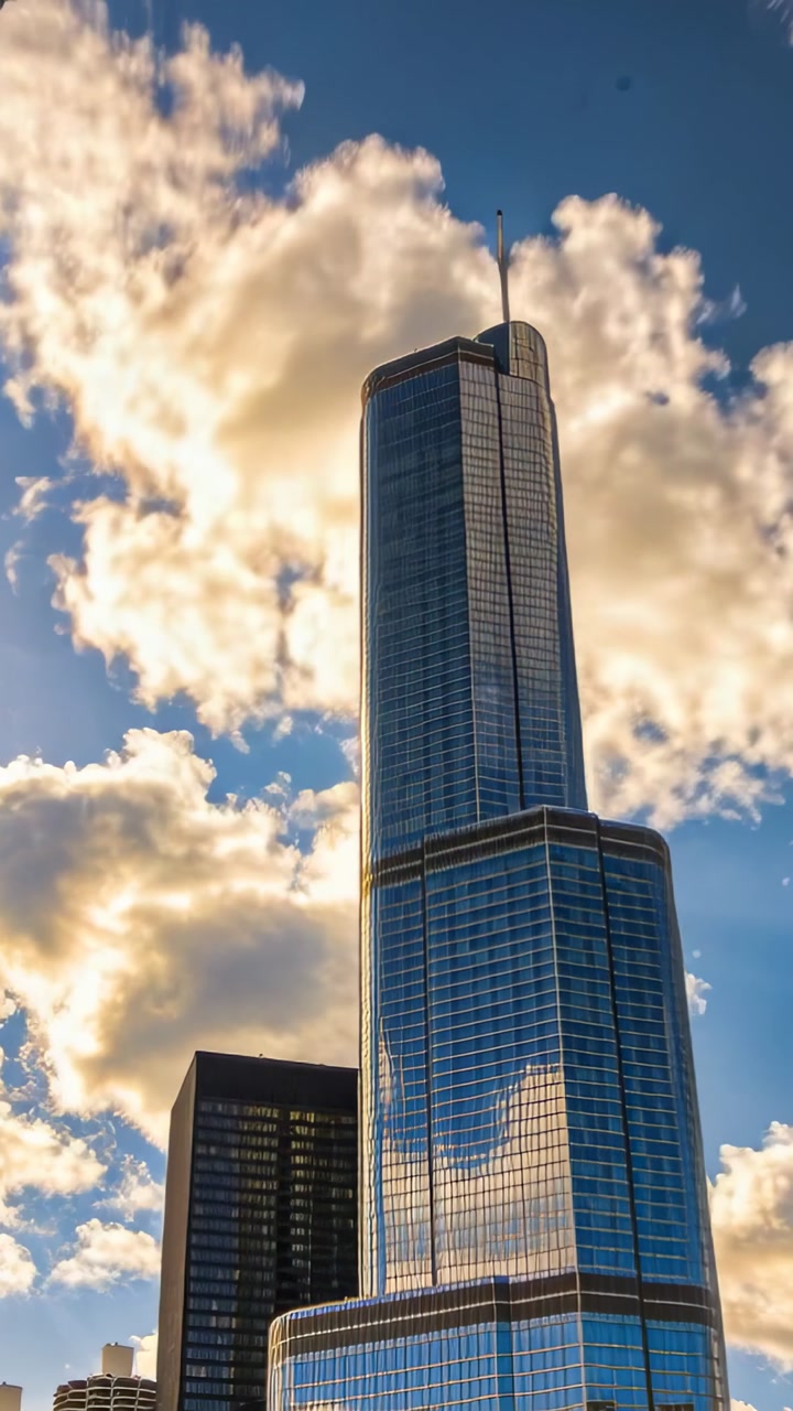 Vertical video: Showing glass tower catching clouds drifting at street, spire and dark tower left
