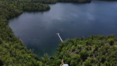 a stunning view of lake matano, surrounded by lush green forest and a wooden jetty, in sulawesi, indonesia - aerial drone shot