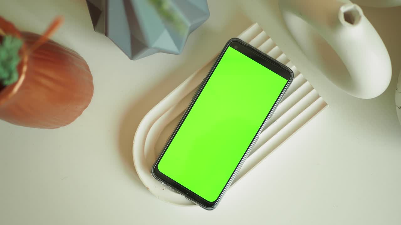 teléfono inteligente con pantalla verde en mesa blanca con decoración