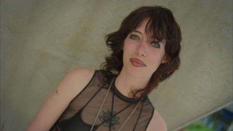 outdoor fashion portrait of young alternative style woman with tattoos and piercing shaking head standing outside modern buildings shot in real time