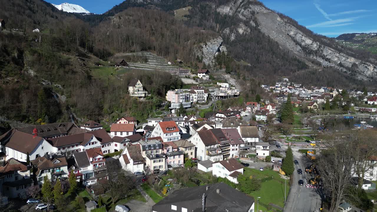 clip de avión no tripulado que muestra edificios blancos tradicionales en los alpes suizos, al lado de un lago tranquilo, en un día soleado de primavera