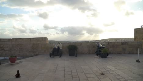 Cañones-Frente-A-La-Ciudad-De-Victoria-Desde-Las-Murallas-Defensivas-De-La-Fortaleza-De-Cittadella-Con-Rayos-De-Sol-Brillando-A-Través-De-Las-Nubes