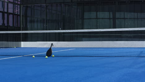 Padel tennis racket and balls on blue indoor court near net, ready for play, copy space