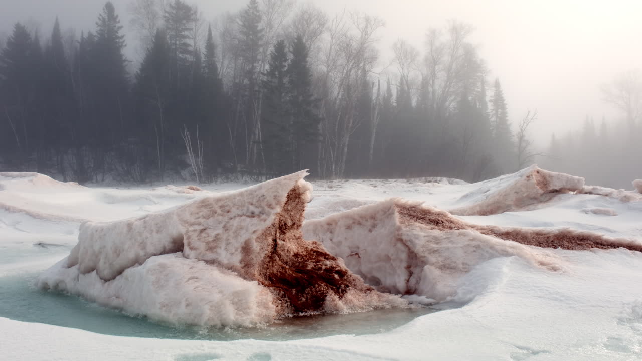 Store frosne isflager langs den sneklædte kystlinje ved Lake Superior med en tåget vinterkov i baggrunden
