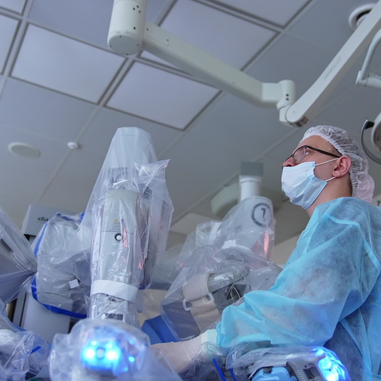 Surgeon in mask monitoring the work of robotic equipment. Advanced technology equipment in modern operation theatre. Low angle view
