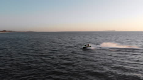 a woman rides a jet ski at high speed on an open ocean at sunset, drone tracking shot