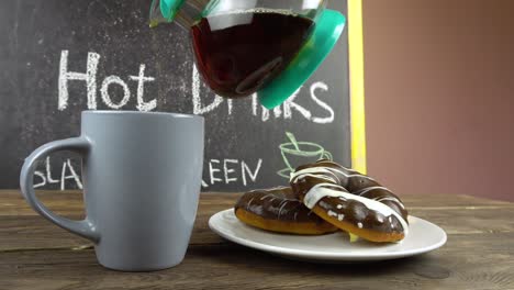 a cup of tea and donuts in chocolate glaze on a cafe table.tea is pouring from a transparent teapot.