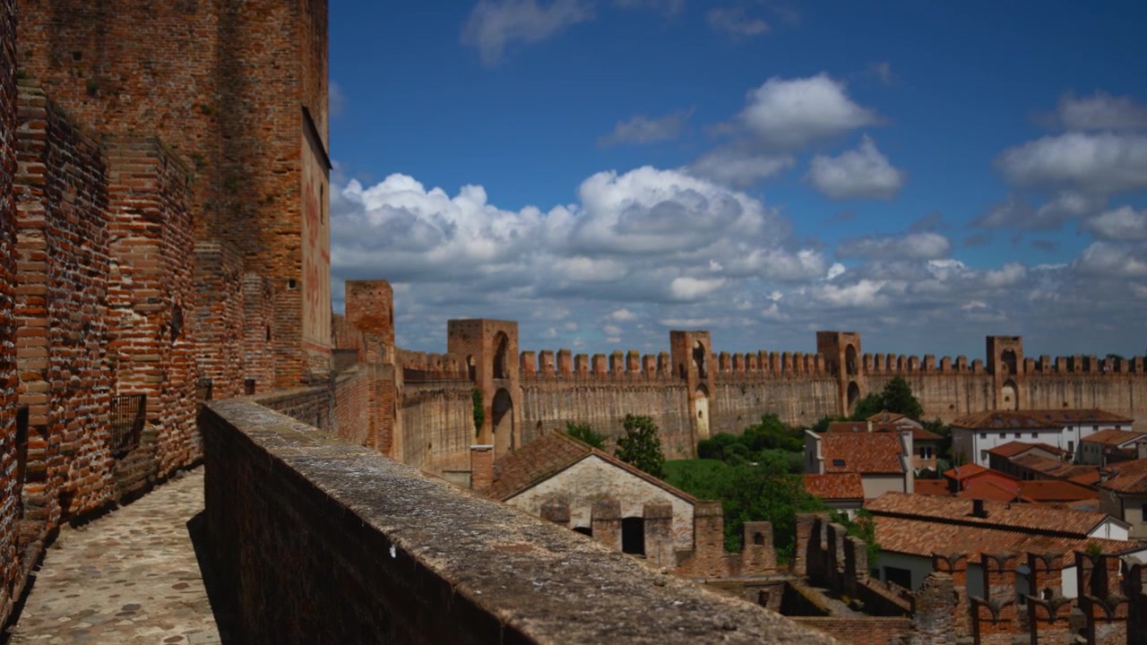 Primo piano di strutture in mattoni medievali stagionate sulla cinta muraria della Cittadella con il centro storico sullo sfondo