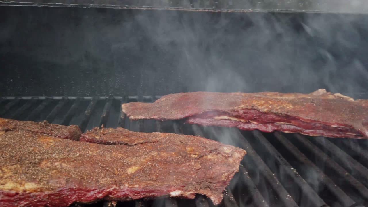 Slider shot seasoned beef navel brisket cooking on grill of meat smoker
