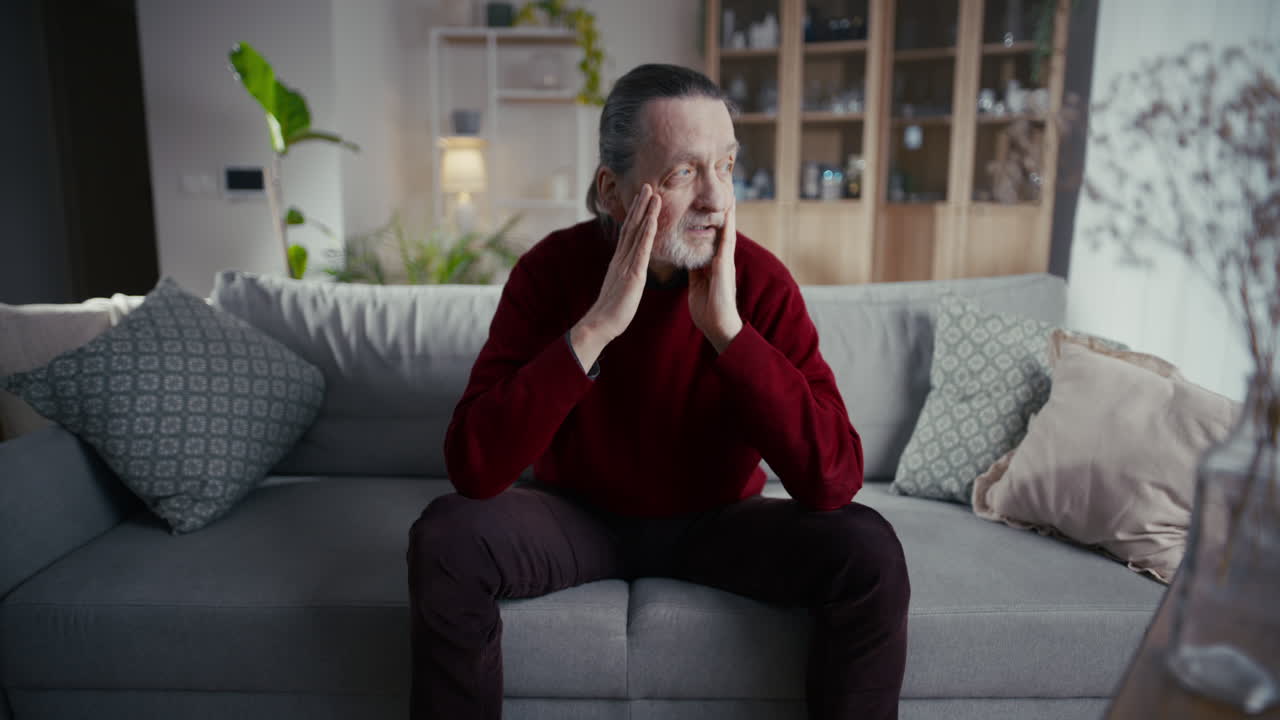 Elderly Man Sitting Thoughtfully on a Couch in His Living Room
