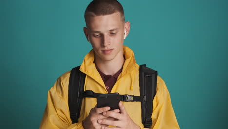 Young-blond-guy-with-backpack-using-smartphone