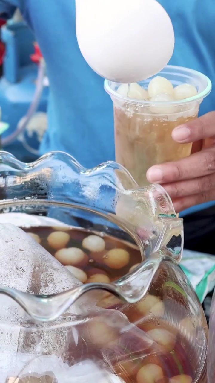 A street vendor scoops sweet longan fruit and syrup into a cup with ice.