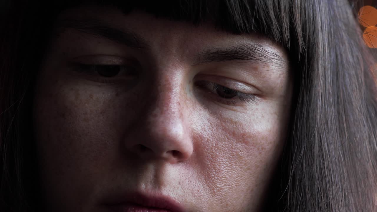 그녀가 생각하고 아래를 내려다 보면서 갈색 머리와 앞머리가있는 주근깨가있는 갈색 눈의 소녀를 클로즈업