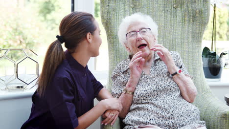 senior woman sitting in chair and talking with nurse in retirement home