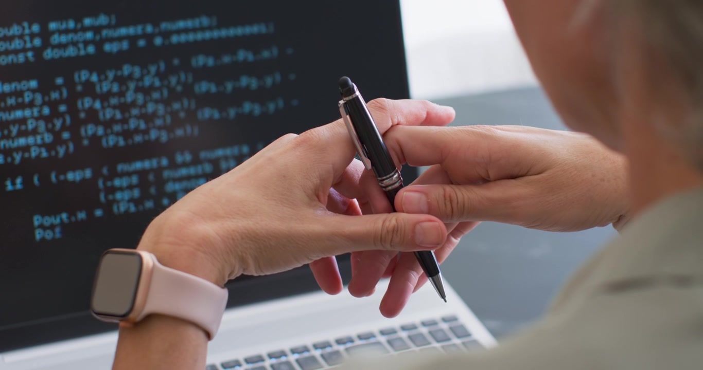 Kvindelig koder ved skrivebord ser kode på bærbar computer, justerer sort kuglepen og smartwatch, løfter for at pege