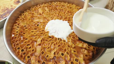 the cook pours yogurt on the turkish ravioli with a wooden spoon