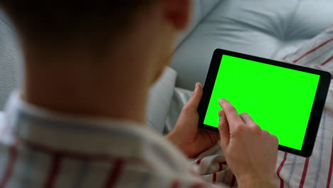 gerente con una tableta de pantalla verde en primer plano. hombre desconocido trabajando en casa remotamente.
