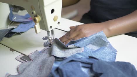 a slow motion close up shot of an african woman's hands pushing material through an electric sewing machine