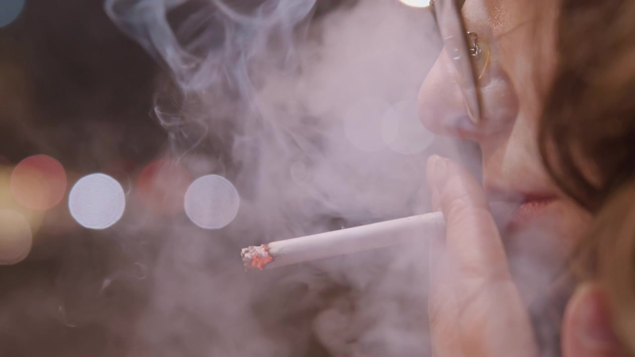 Artista en la vida nocturna. Ambiente urbano capturado con un artista fumando bajo luces de neón. Escenario nocturno que muestra a un artista relajándose e inhalando humo en medio de una colorida iluminación urbana.