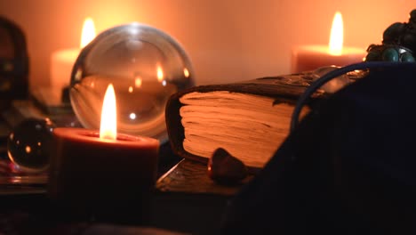 Background-of-a-fortune-teller-table-covered-with-fabric,-with-crystal-balls,-stones,-cards,-ancient-books,-rings-and-candles-with-flickering-flames