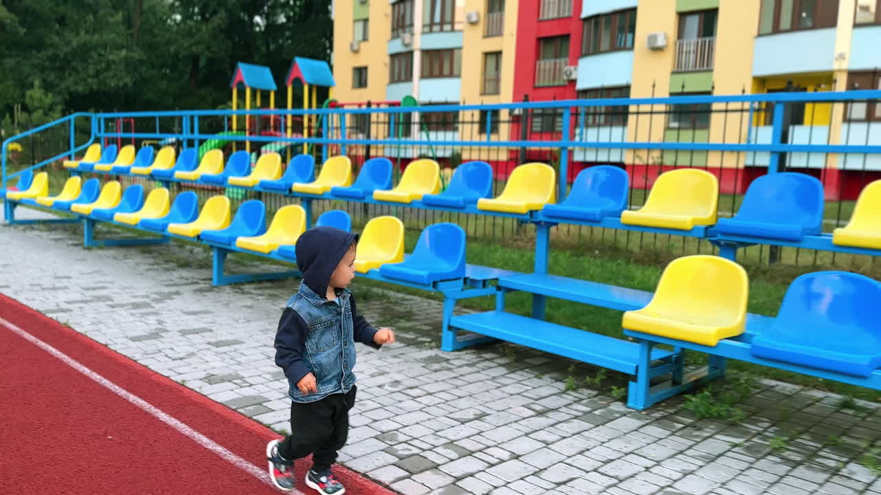 Lovely year old baby is on the walk. Child goes along the rows of seat at the stadium.