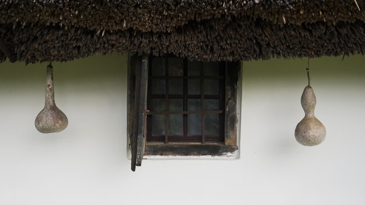 Small rustic window with dried gourds hanging under thatched roof