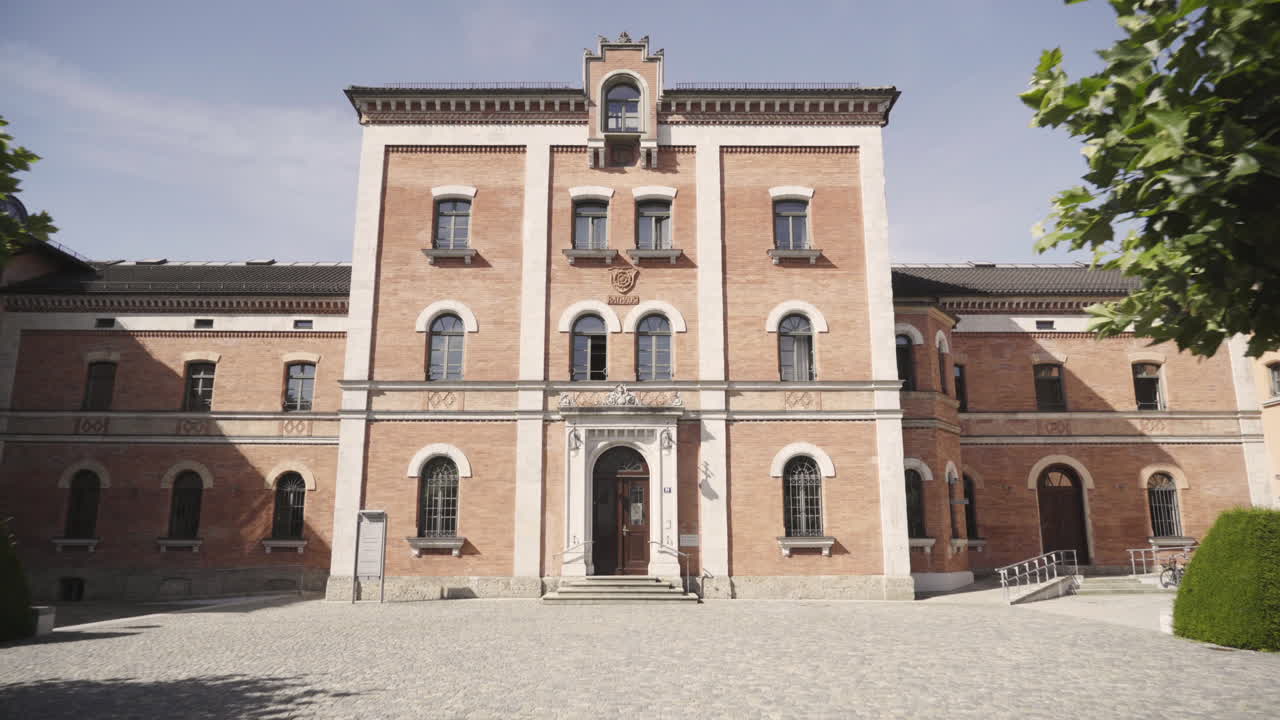 Smooth gimbal shot of the old city hall of rosenheim with
it’s very interesting looking brick wall architecture,
European style building and green trees in front of the
house