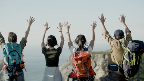 back view of family standing on cliff edge, raising their arms and enjoying the view