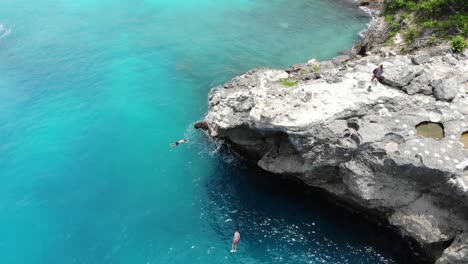 drone footage of two cliff jumpers jumping at the same time into ocean blue lagoon, indonesia