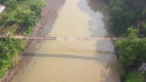 aerial drone shot of dirty river with dangerous wooden bridge in tropical landscape of indonesia