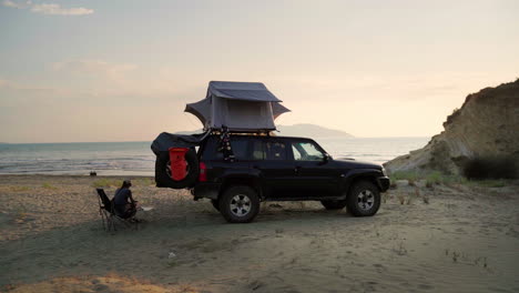 woman sitting on a chair by her car on the beach