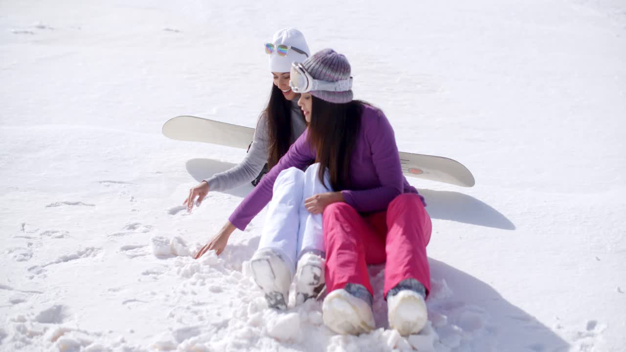 dos mujeres jóvenes sentadas charlando en la nieve