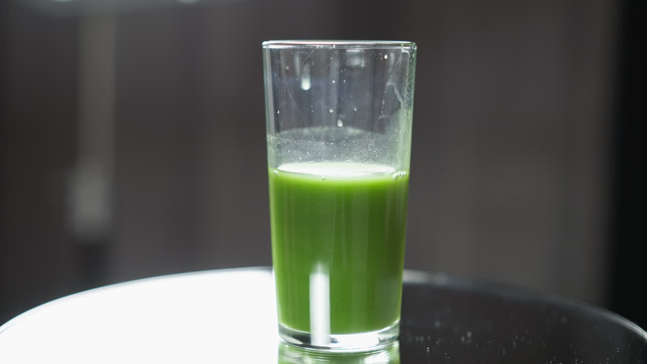 vaso de jugo de verduras verdes con tapa espumosa en la superficie reflectante, enfoque suave