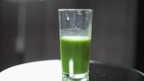 glass of green vegetable juice with frothy top on reflective surface, soft focus