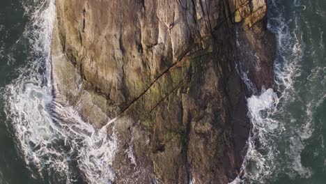 drone top view going close to a rock where the waves come and go