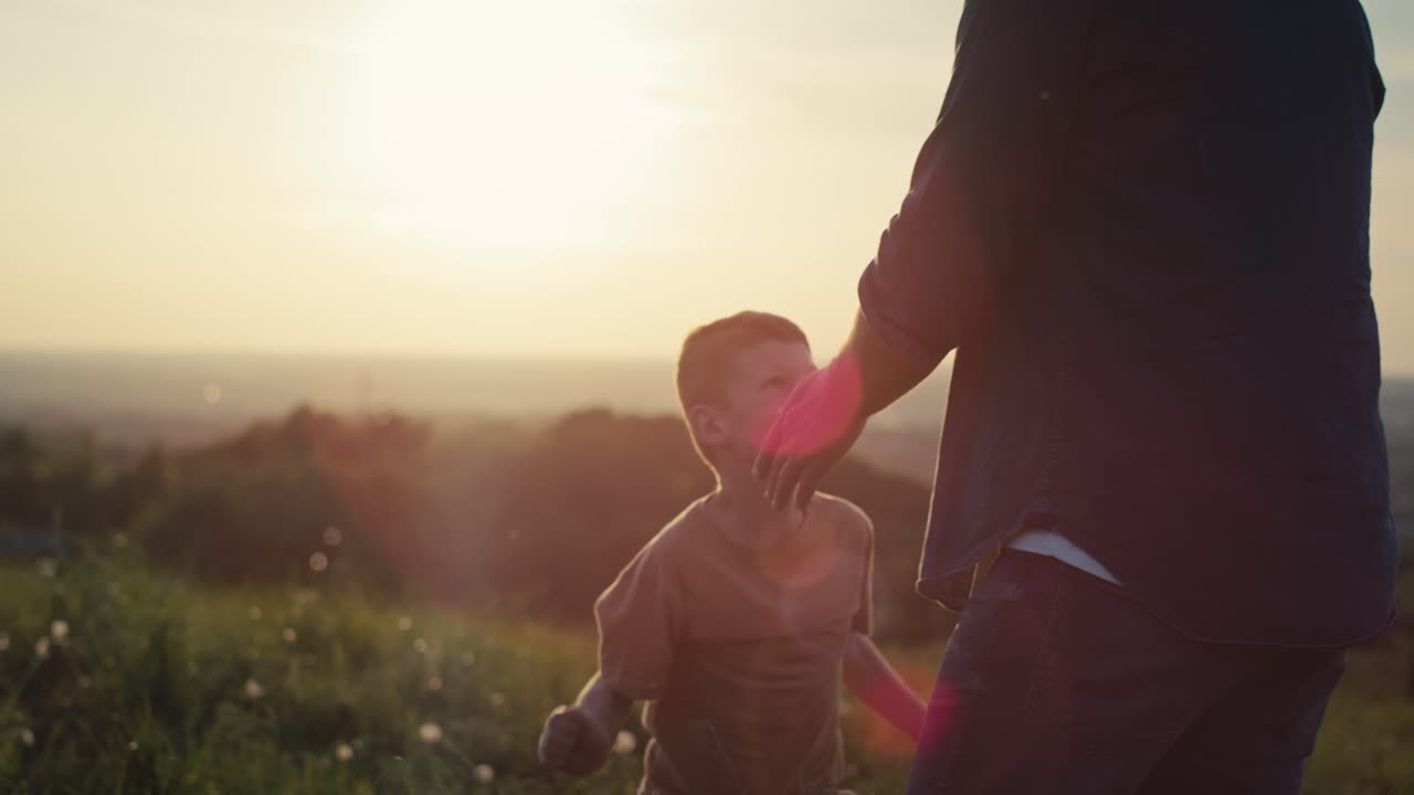 un niño corriendo por su padre en el prado durante la puesta de sol.
