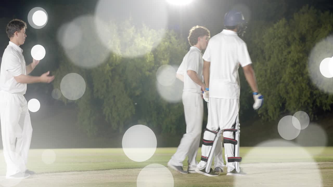 Cricket-hold jubler efter wicket på banen, linse-bokeh over spillere, handsker justeres, batter går