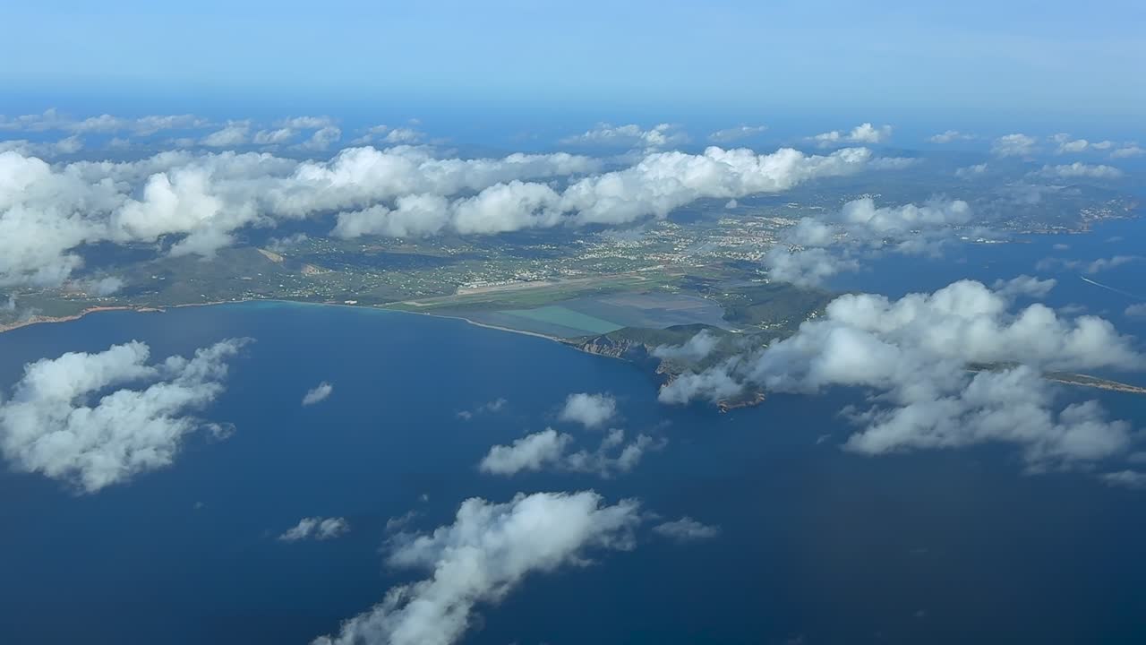 A left side aerial view of Ibiza Island, with a view of the airport and city, under few clouds in a bright summer morning