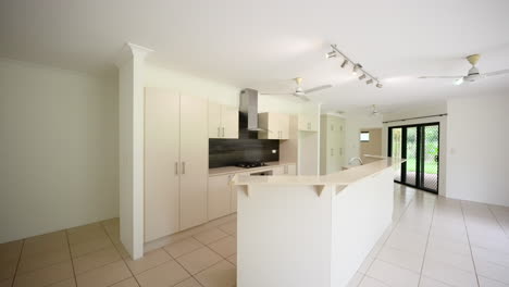 vacant empty large modern kitchen home interior with ceiling fans and dark backsplash in beige off-white apartment