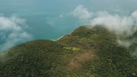 antena de drones sobre nubes que muestran bosque tropical en una isla con agua azul