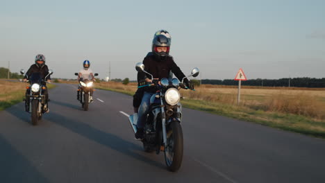 a group of bikers drives along the highway among the fields on a clear autumn day