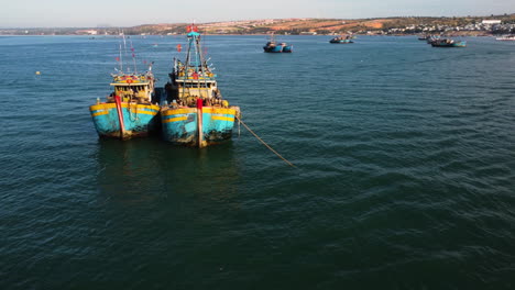 Una-Toma-Aérea-De-Dos-Coloridos-Barcos-De-Pesca-Anclados-En-La-Bahía-De-Mui-Ne,-Vietnam