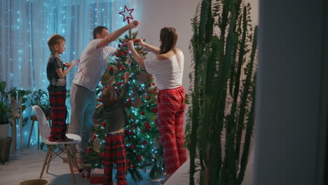 feliz familia preparándose para el año nuevo vacaciones de invierno concepto de celebración. joven pareja de 30 años su preescolar adorable dos hijos decorando árbol de navidad crear un ambiente festivo en una casa acogedora moderna. imágenes de alta calidad 4k