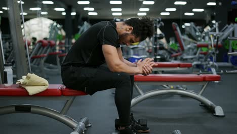 el hombre sentado y respirando después de terminar el curso de entrenamiento con pesas en el gimnasio, vista lateral