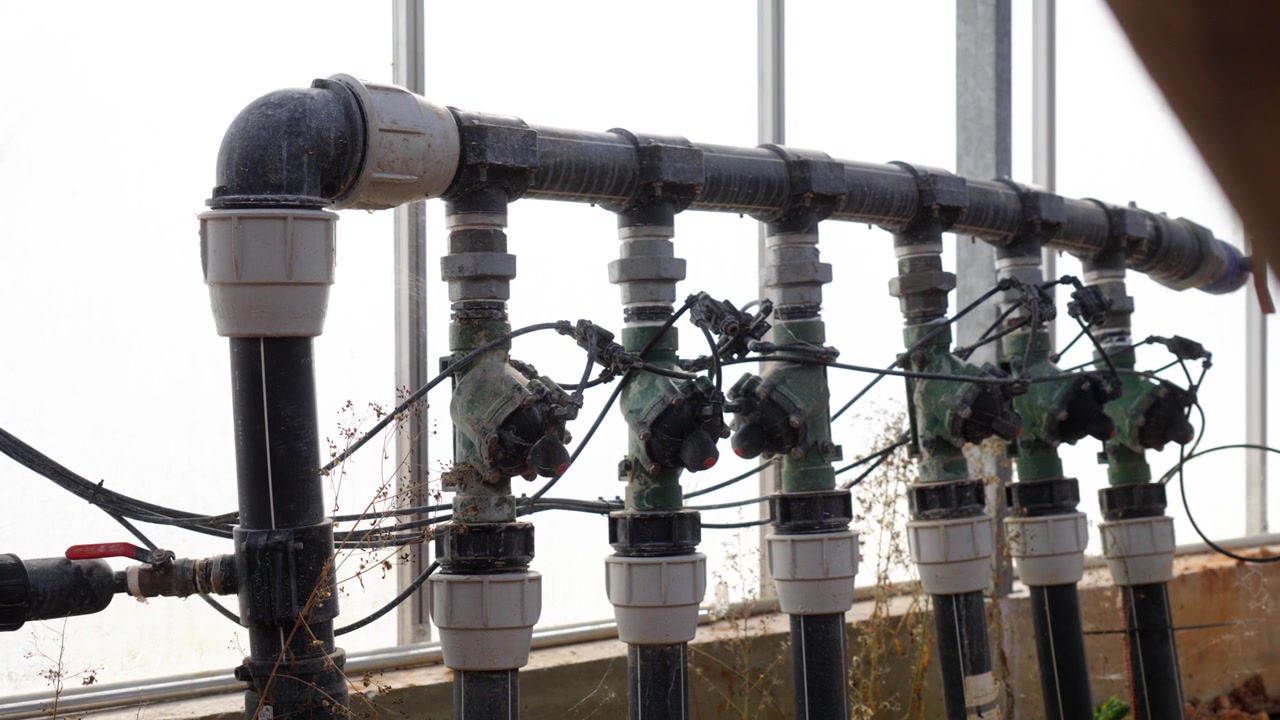 Close-up of irrigation pipes and control valves inside greenhouse agricultural system, reveal past foreground